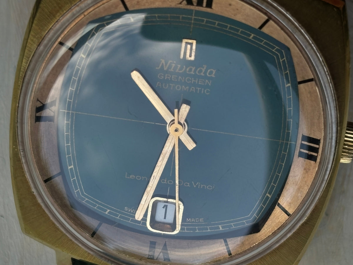 Close-up of signed Nivada Grenchen automatic green dial with gold hands and Roman numeral chapter ring
