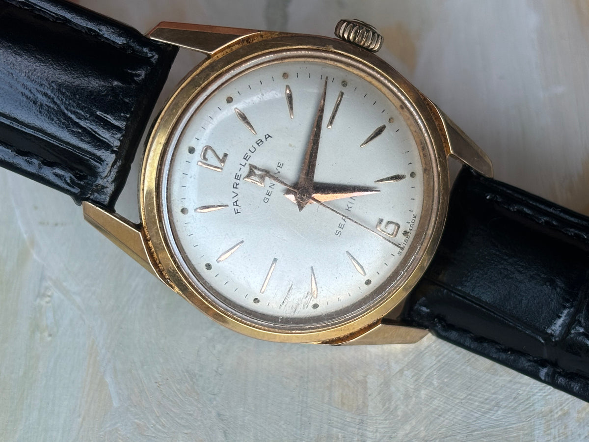 Angled front view of a vintage Favre-Leuba Genève Sea King watch with a silver dial and black leather strap.