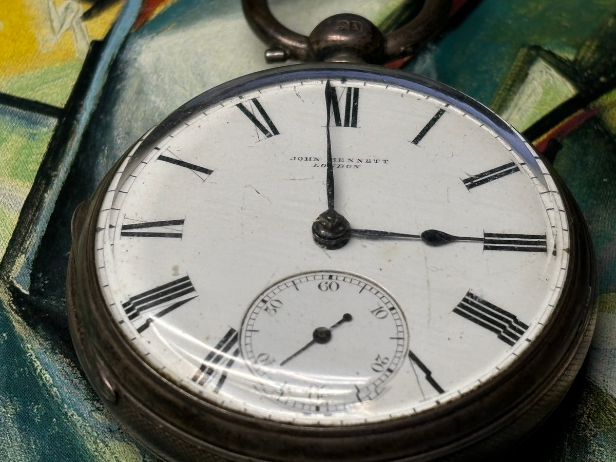 Close-up of an antique John Bennett London pocket watch with white dial and black Roman numerals.