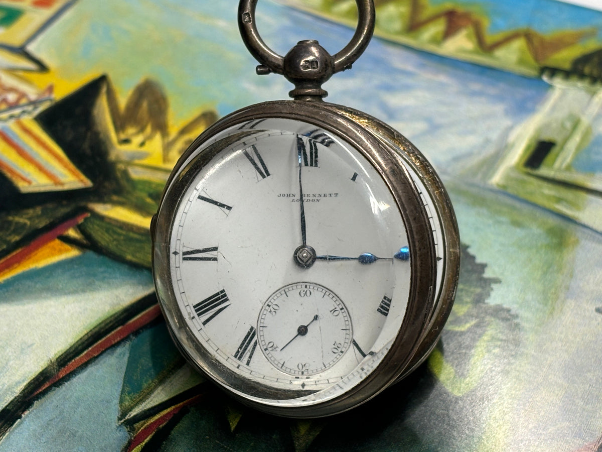 Full view of an antique John Bennett London pocket watch on a painted background.