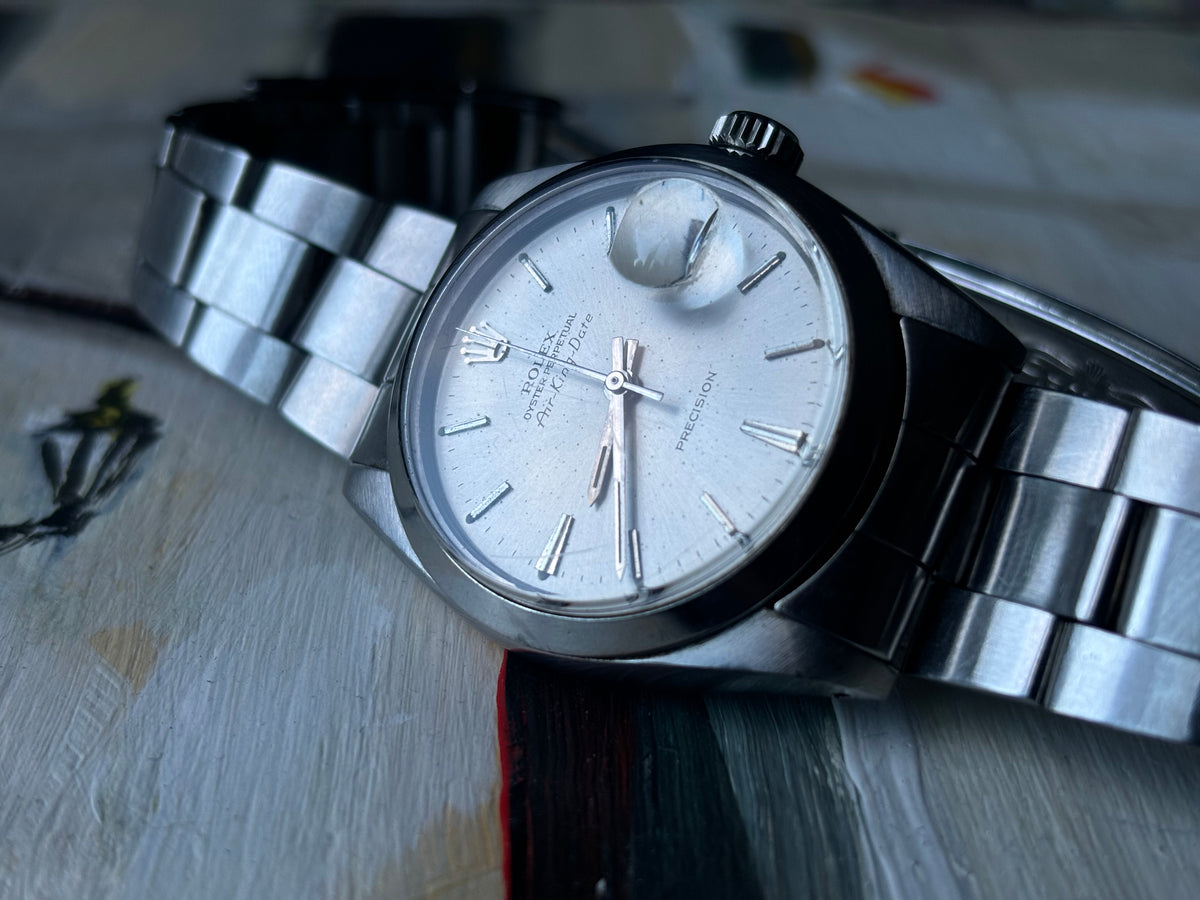 Vintage Rolex Air-King-Date Precision ref. 5700 with silver sunburst dial and Oyster bracelet on painted background