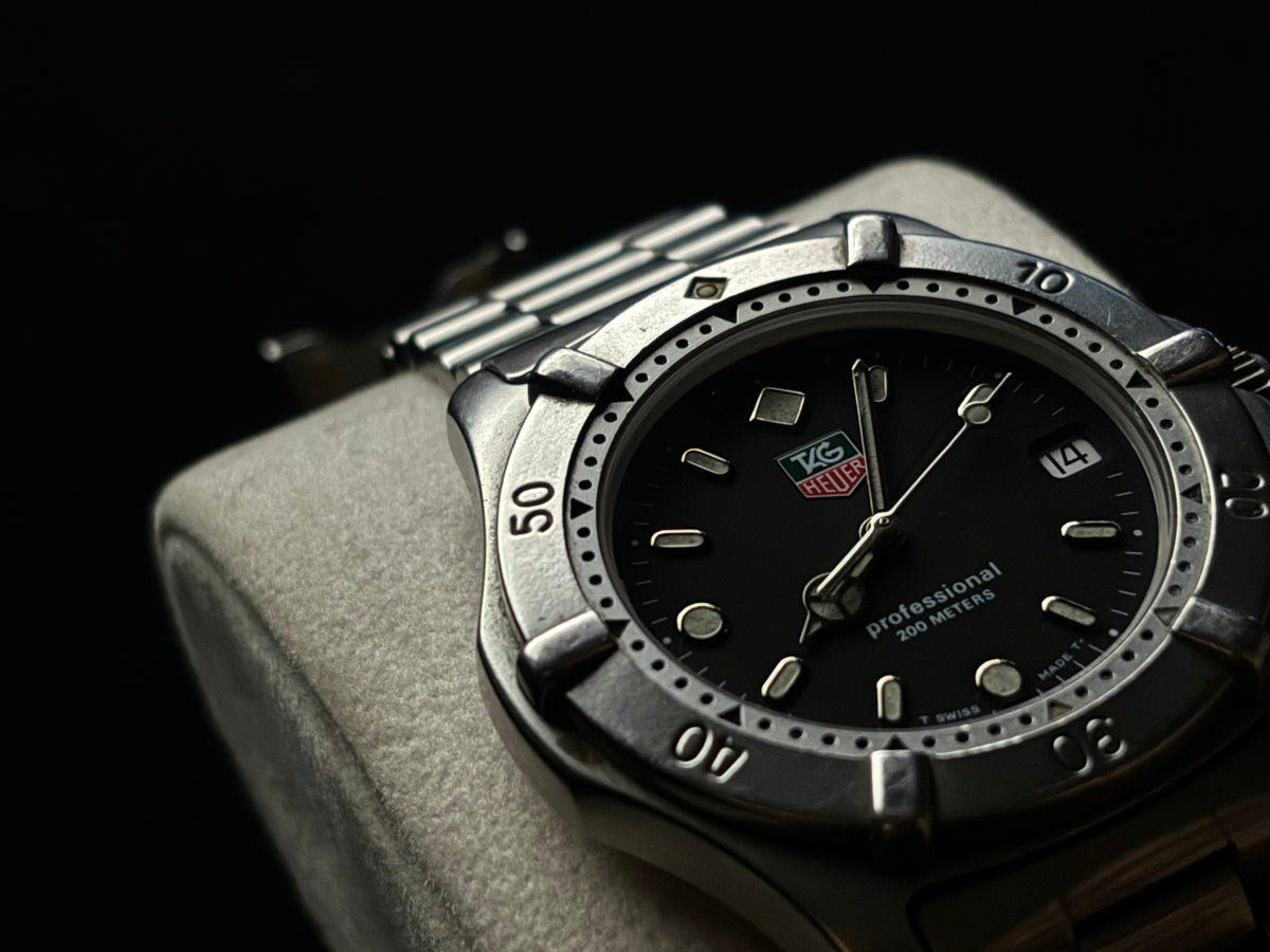 Low-light front view of a vintage TAG Heuer Professional 200 Metres watch with black dial.