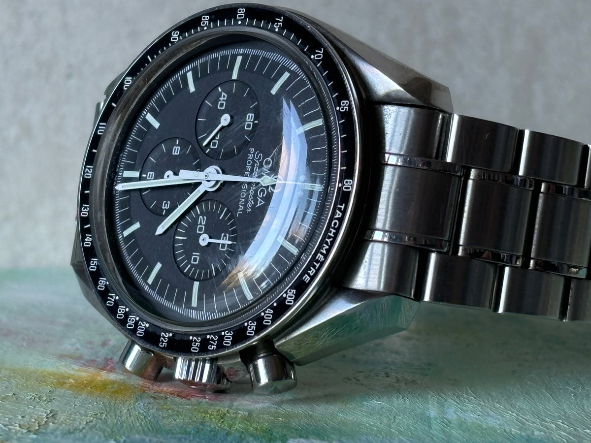 Close-up of an Omega Speedmaster Professional Moonwatch black chronograph dial and stainless-steel bracelet.