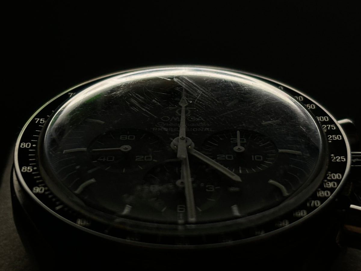 Low-light close-up of an Omega Speedmaster Professional Moonwatch dial and tachymeter bezel.