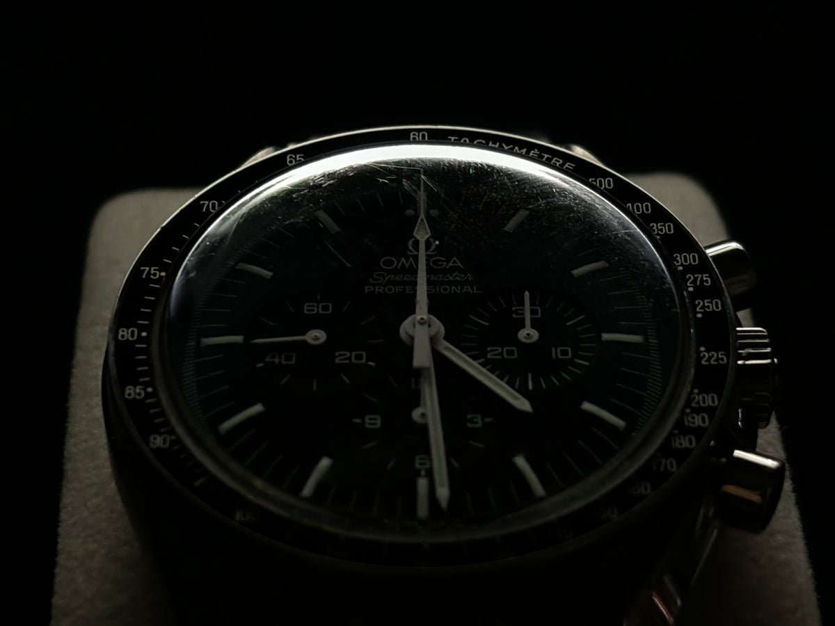 Low-light front view of an Omega Speedmaster Professional Moonwatch with black dial and tachymeter bezel.
