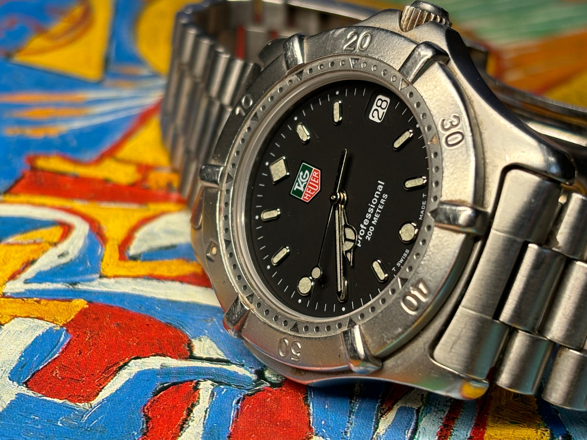 Angled view of a vintage TAG Heuer Professional 200 Metres watch with black dial and date window.